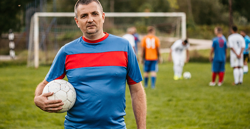 A middle aged white male looks on whilst holding a football